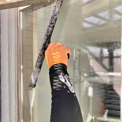 高所作業員がロープで窓ガラスを清掃中。外壁の黒ずみや水垢を除去。