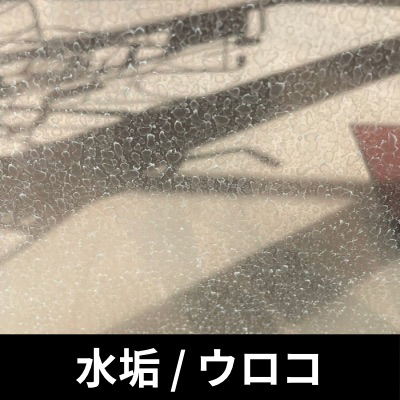 ガラス表面に付着した白い水垢・ウロコ汚れ。硬水成分のカルシウムやシリカが固着し、通常清掃では落ちない状態を示す。