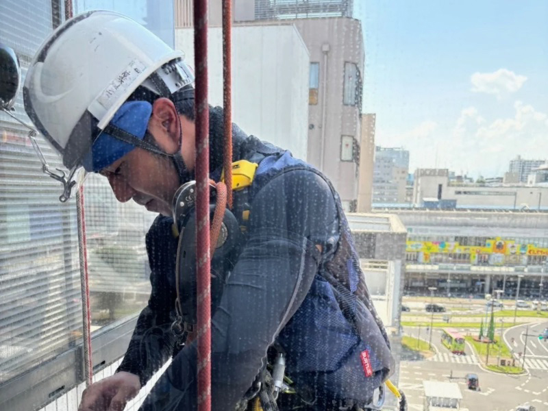 高所ロープ作業でビルの窓ガラスを再生研磨し、水垢を除去している作業中の様子