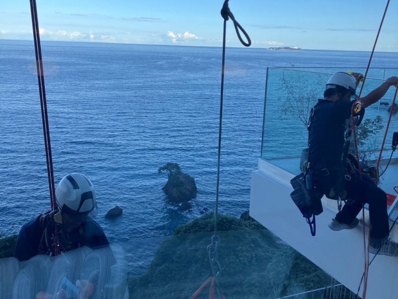 高所ガラス研磨作業中の様子。安全ロープで作業しながら塩害汚れを除去