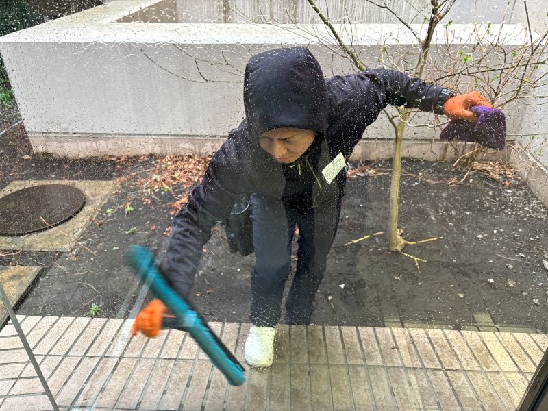 ガラス専用洗剤を塗布するシャンパー作業。油膜を浮かせて、スクイジーで一気に拭き取るプロの技術。