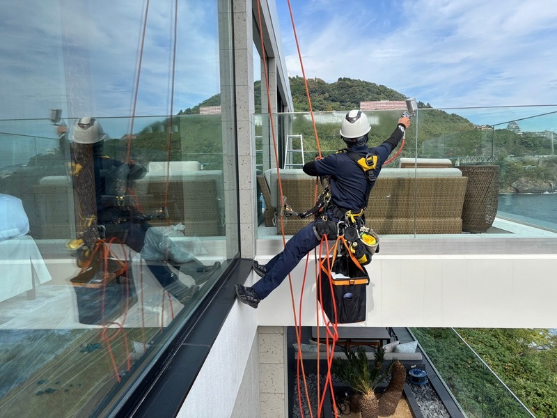 静岡県の海沿いホテルで高所の窓ガラスに光触媒コーティングを施工している様子。ロープ作業で安全に塗布をおこなっている。