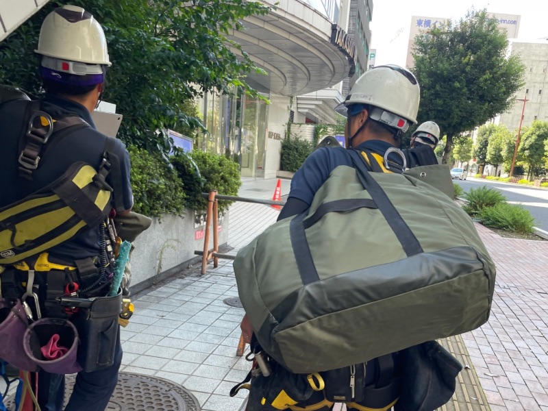 高所窓ガラス清掃で使用するロープを持って屋上へ向かう作業員